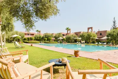 a resort with a swimming pool with chairs and a table at Les Jardins De Zyriab in Aït Hamid