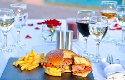 a sandwich and french fries on a table with wine glasses at Les Jardins De Zyriab in Aït Hamid