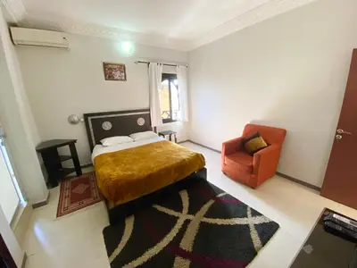 a bedroom with a bed and an orange chair at Hôtel Narjisse in Marrakech