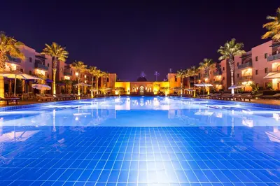 a large swimming pool at night with palm trees and buildings at Jaal Riad Resort Adults Only in Marrakech