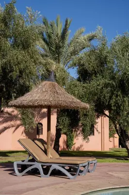 a lounge chair with a straw umbrella next to a pool at Maison Ayda in Marrakech