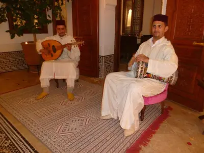 two men are sitting in chairs playing instruments at Riad Viva in Marrakech