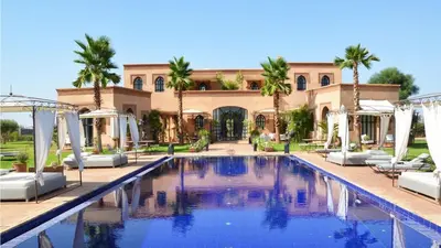 a pool in front of a building with palm trees at Palais Lona in Marrakech