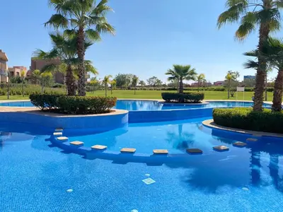 a large swimming pool with palm trees in a resort at Marrakech golf city prestigia in Marrakech