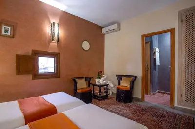 a hotel room with two beds and a table and chairs at Riad l'Heure d'Eté in Marrakech