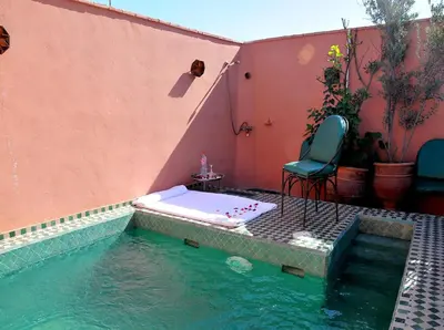 a swimming pool with a table and a chair next to a house at Riad Lila in Marrakech