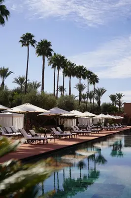 a pool with chairs and umbrellas and palm trees at Selman Marrakech in Marrakech