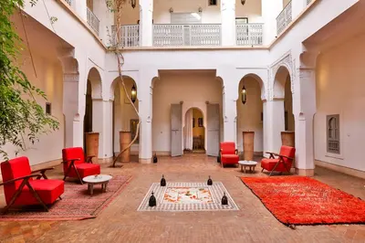 a courtyard with red chairs and tables and a rug at Hotel & Spa Riad Al Jazira in Marrakech