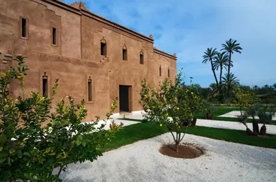 a large brick building with trees in front of it at Hotel Les Cinq Djellabas in Douar Caïd Layadi