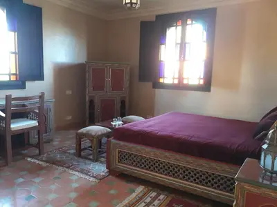 a bedroom with a bed and a table and windows at L'OLIVERAIE DE L'ATLAS in Marrakech