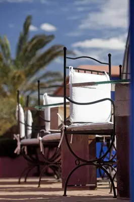 two chairs and a glass table with palm trees in the background at Le Farnatchi in Marrakech