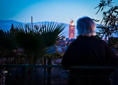 a woman sitting on a bench looking at a clock tower at Riad Cherihane in Marrakech