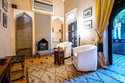 a living room with two white chairs and a fireplace at Dar Les Cigognes in Marrakech