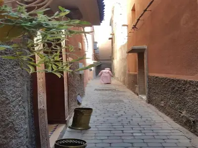 a woman walking down an alley in a pink coat at Riad Maison Aicha in Marrakech