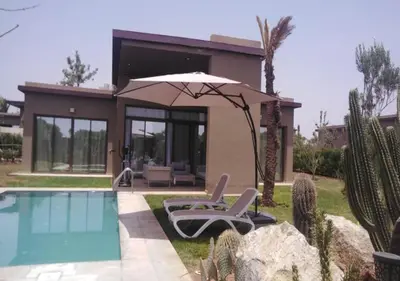 a house with a pool and two chairs and an umbrella at Palms Edge Villas avec Piscine & Jardin Privés in Marrakech