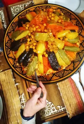 a plate of food with a person holding a knife at Riad Basma Marrakech in Marrakech
