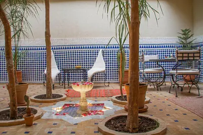 a room with palm trees and chairs and tables at Riad Dar Tamlil in Marrakech
