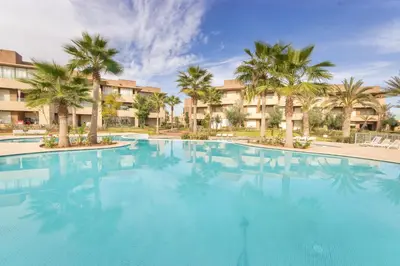 a large swimming pool with palm trees and buildings at Vue époustouflante sur L Atlas - Prestigia in Marrakech