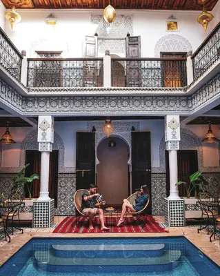 two men sitting in chairs next to a swimming pool at Riad Medina Art & Suites in Marrakech