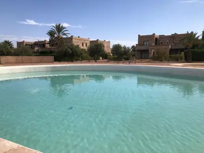 a large pool of blue water in front of houses at Villa Mayrit, Villa estilo Riad en un entorno único in Marrakech