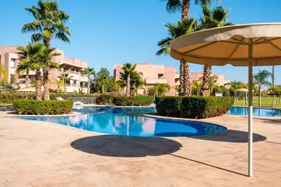 a pool at a resort with an umbrella and palm trees at Coup de cœur à Marrakech - idéal famille et couple in Marrakech