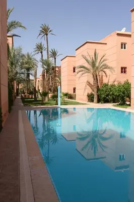 a swimming pool with palm trees and a building at Résidence alqaria assiyahiya full private riad in Marrakech