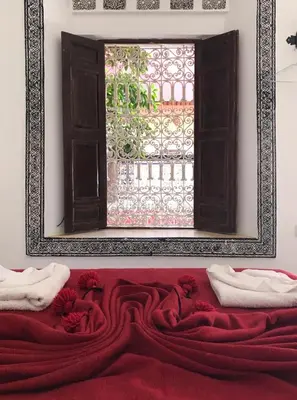 a window in a room with a red blanket and a mirror at Riad Naya in Marrakech