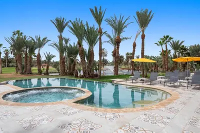 a pool with palm trees and chairs and umbrellas at Palmeraie Golf Suites By Pickalbatros in Marrakech