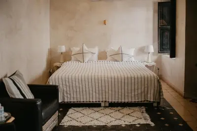 a bedroom with a bed with a striped comforter and a chair at Riad Alnadine in Marrakech