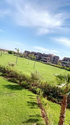 a green field with palm trees and buildings in the background at Comme a la maison Prestigia Golf acces piscine in Marrakech