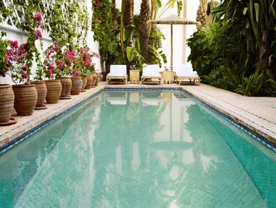 a swimming pool with chairs and flowers and plants at Riad L'Hôtel Marrakech in Marrakech