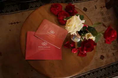 a wooden table with a vase of flowers and a red envelope at Riad white flowers in Marrakech