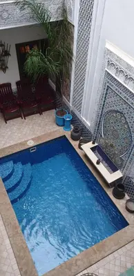 a large blue swimming pool in a room with chairs at Riad Nouhal in Marrakech