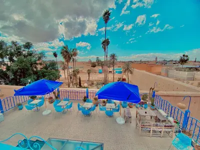 a patio with blue umbrellas and tables and chairs at Hostel Essassi 23 in Marrakech