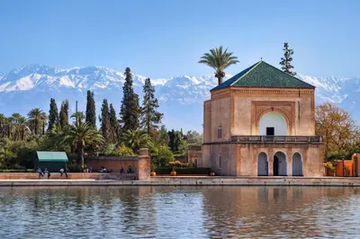 a building next to a lake with mountains in the background at Appartement Nour 5 Marrakech Centre Gueliz avec piscine in Marrakech