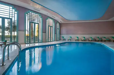 a swimming pool in a hotel with chairs and windows at Grand Mogador Agdal & Spa in Marrakech