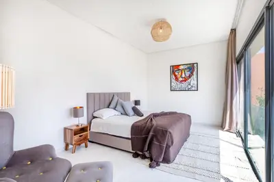 a white bedroom with a bed and a chair at Villa Nounja Golf Amelkis Marrakech in Marrakech