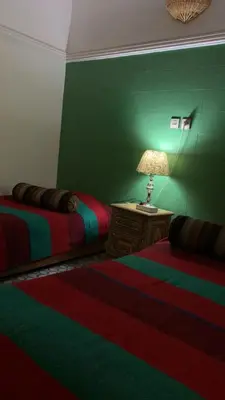 a green room with two beds and a table with a lamp at Riad taddert in Marrakech