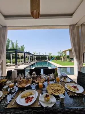 a dining table with food and a pool in the background at Villa Le Clos de l'Atlas in Marrakech