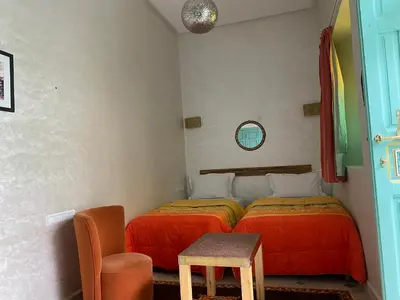a bedroom with two beds and a table and a chair at Riad Deux Palmiers in Marrakech