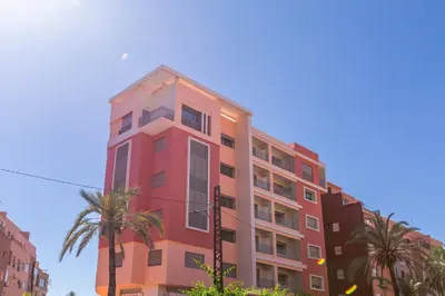 a pink building with palm trees in front of it at ZARI Boutique ApartHotel in Marrakech