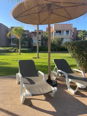 two lounge chairs under an umbrella on a patio at Appartement de luxe Prestigia Opale in Marrakech