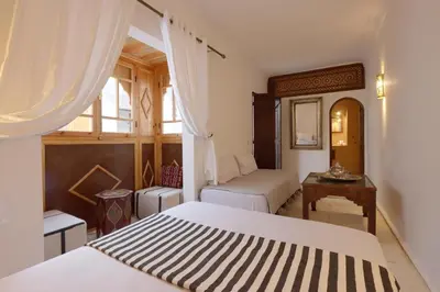 a bedroom with two beds and a desk and a window at Riad Jenan L'mouassine in Marrakech