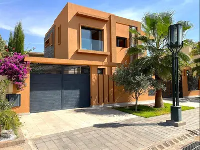 a house with a garage and a palm tree at Belle et spacieuse villa au Golf Amelkis Marrakech in Marrakech