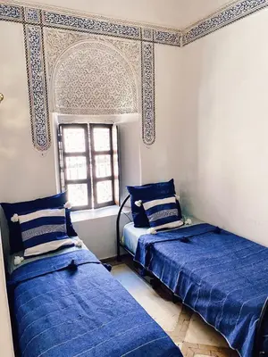 two beds in a room with blue sheets and a window at Riad Sidi Radoine in Marrakech