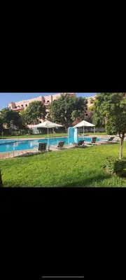 a swimming pool with chairs and umbrellas in a park at appaartement M23 premium village in Marrakech