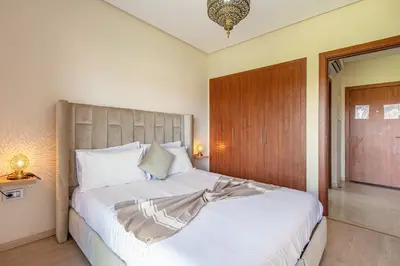 a bedroom with a large white bed with a wooden headboard at Perle Rare a Prestigia - Vue Sur Golf in Marrakech