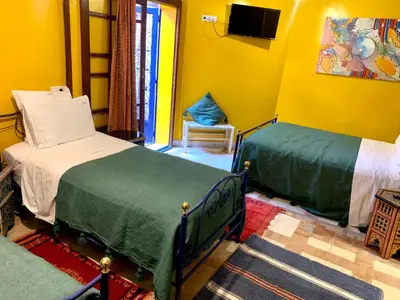 a bedroom with two beds and a tv on the wall at Riad Mazal in Marrakech