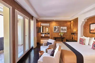 a hotel room with a bed and two chairs at Hôtel & Ryads Barrière Le Naoura in Marrakech