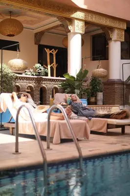two people laying in beds next to a swimming pool at Amani Hotel Suites & Spa in Marrakech